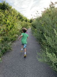 Rear view of boy running on footpath amidst plants