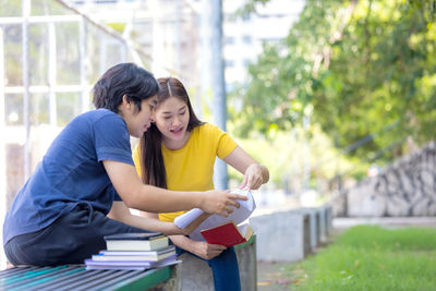 Couple of students are studying together, and a teenager sits on a seat beside court with a book..