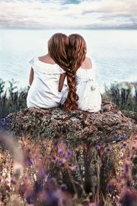 Rear view of woman sitting on shore against sky