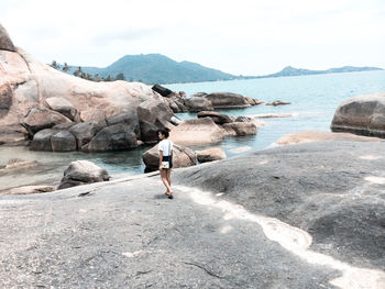 Woman on rock at beach against sky