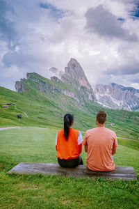 Rear view of men sitting on mountain against sky