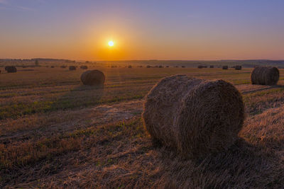 Hay bales on field against sky during sunset