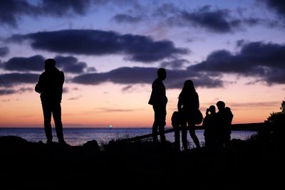 Silhouette people standing at beach during sunset