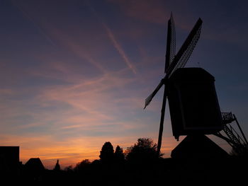 Low angle view of traditional windmill against sky at sunset