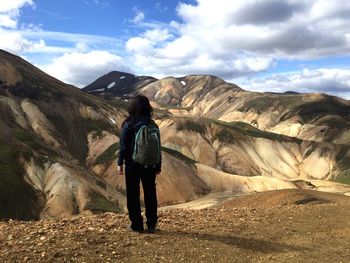 Rear view of woman standing on rock against sky