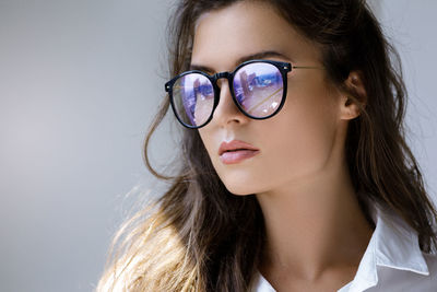 Close-up of young woman wearing sunglasses against wall