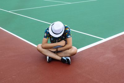 High angle view of man wearing hat while sitting on tennis court