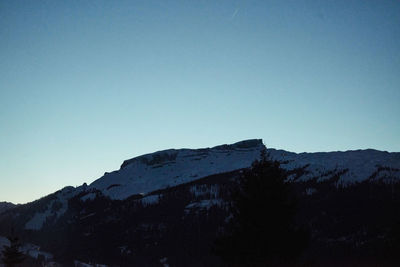 Low angle view of snowcapped mountains against clear blue sky