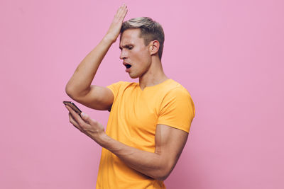 Portrait of young woman suffering from mobile phone while standing against yellow background