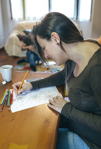 Close-up of woman drawing on paper with family in background at home