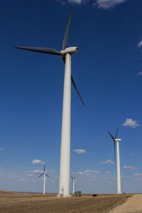 Low angle view of wind turbines on field against sky.