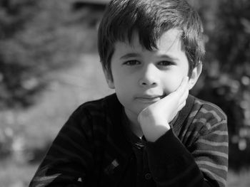 Portrait of cute boy with hand on chin sitting outdoors