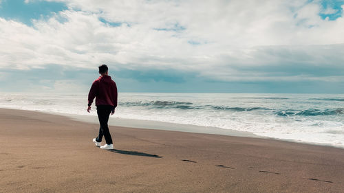 Rear view of man walking on the beach wearing jacket and white shoes