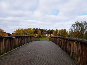 Footbridge over footpath amidst trees against sky