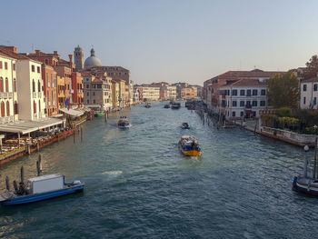 Boats in canal amidst city against clear sky