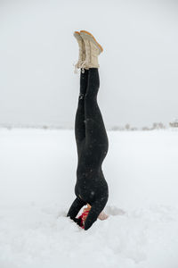 Fit female balancing in salamba shirshasana on snowy meadow while doing yoga in winter