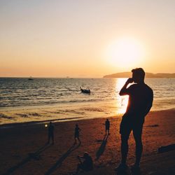 Silhouette people on beach against sky during sunset