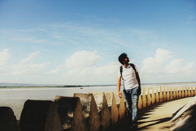 Man standing by retaining wall against sea and sky