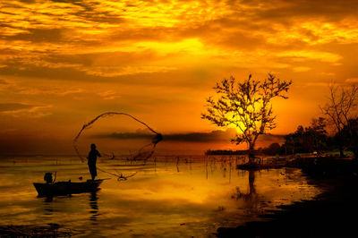 Silhouette people on shore against sky during sunset