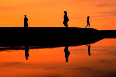 Reflection of people on lake against orange sky