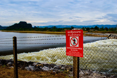 Information sign by lake against sky