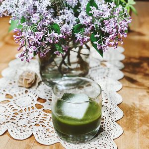 Close-up of green cocktail and vase with flowers on table