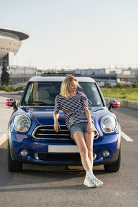 Confident woman auto owner at modern car outside urban buildings of automobile dealership center