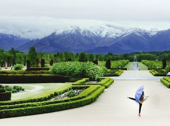 Woman dancing with umbrella in garden against mountains during winter