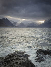 Scenic view of sea by snowcapped mountains against sky