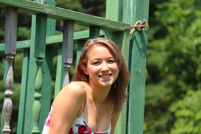 Portrait of smiling woman leaning against green railing on sunny day