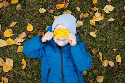 High angle view of boy holding autumn leaves while lying on field