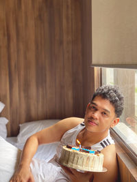 Portrait of man with birthday cake sitting on bed at home