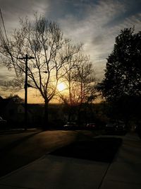 Bare trees against sky at sunset