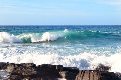 Waves splashing on rocks by sea against sky