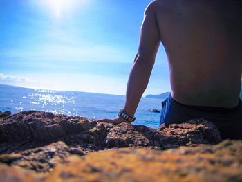 Man on rock at beach against sky