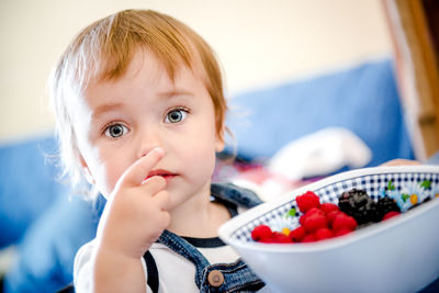 Close-up portrait of innocent baby girl having berries at home