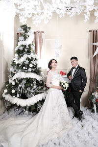 Bride and groom standing against christmas tree at home