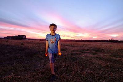 Boy holding lit candles while standing on grassy field at dusk