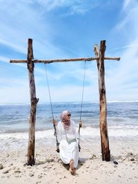 Rear view of woman swinging at beach against sky