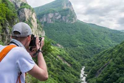 Rear view of man photographing mountains against sky