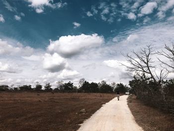 Dirt road amidst field against sky
