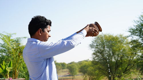 Side view of young man standing against trees