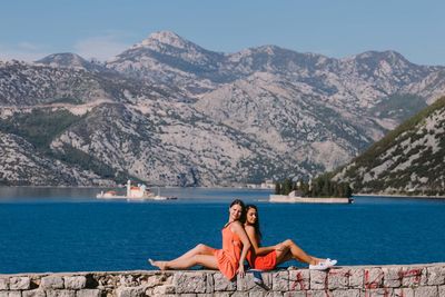 Woman sitting by lake against mountains