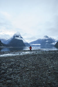 Rear view of man standing by lake and mountains against sky