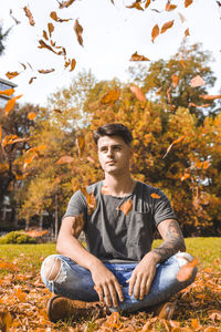 Portrait of young man sitting on autumn leaves