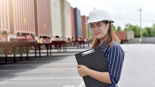 Female engineer holding file while standing by cargo container
