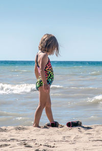 A barefoot child kicks off her shoes and digs her toes into the warm sand on the beach