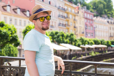 Portrait of young man wearing sunglasses standing against railing