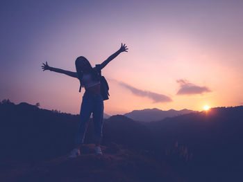 Rear view of silhouette man standing on mountain against sky during sunset