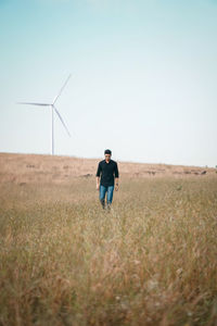 Front view of man walking on field against clear sky and windmill 